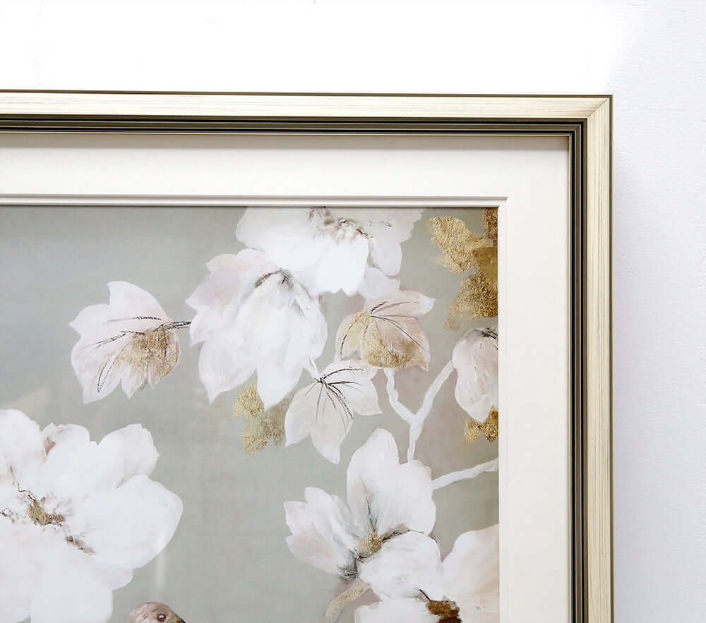Close-up framed wall art with white blossoms, gold accents, and a small bird